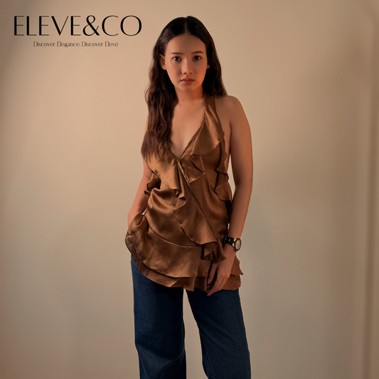 Woman wearing a brown ruffled top and dark jeans against a beige background with 'Eleve&Co' branding.